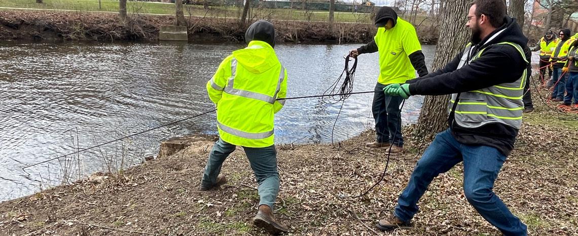 Landscape Services crew use ropes to haul garbage out of the Red Cedar River