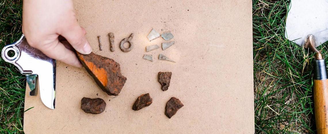 pieces of rusty metal and glass lay next to a trowel on the grass