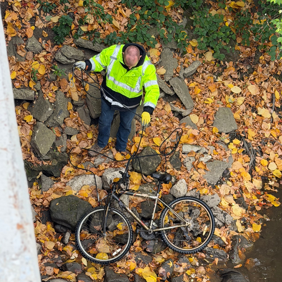 Man wearing a safety vest standing beside a bicycle.