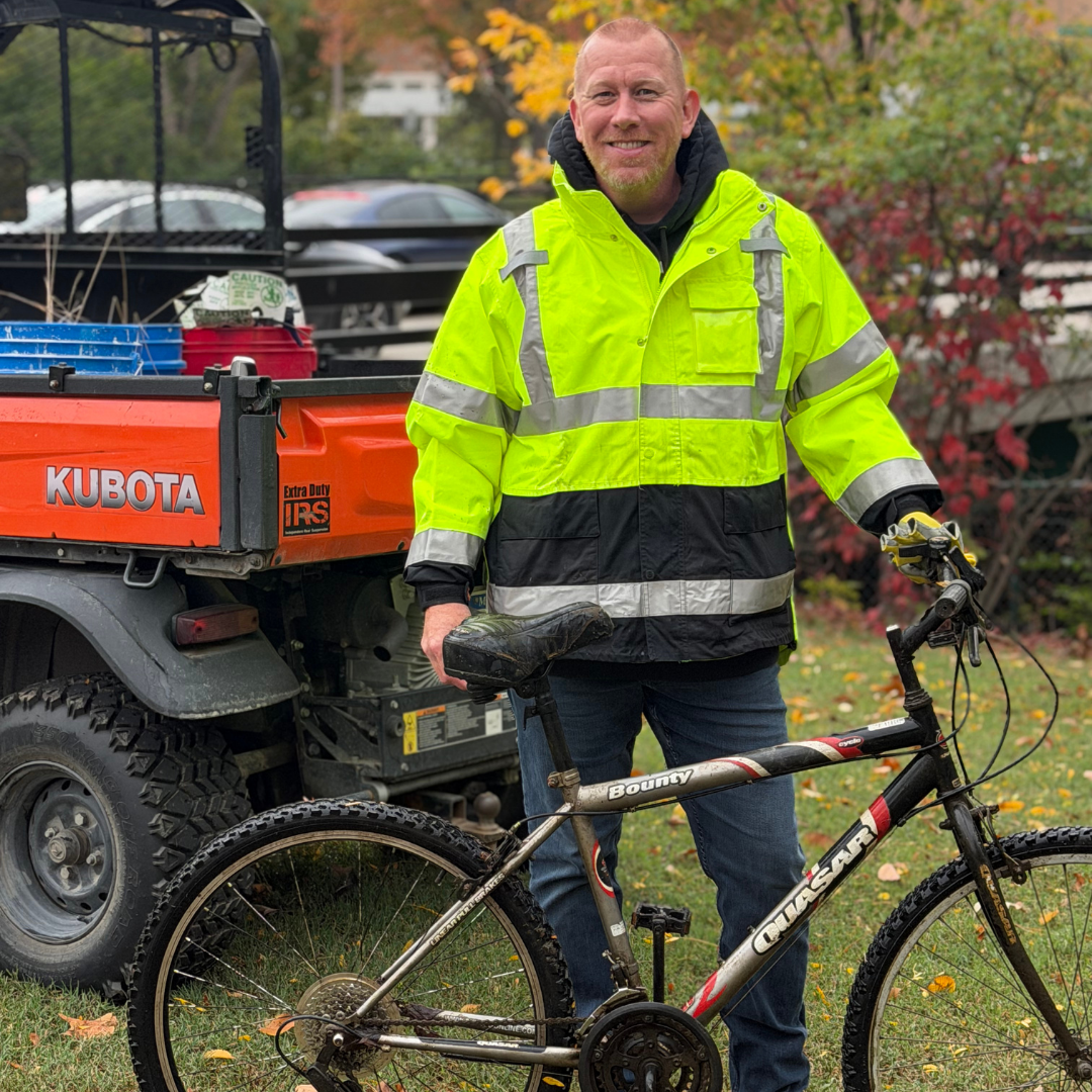 Man wearing a safety vest standing beside a bicycle.
