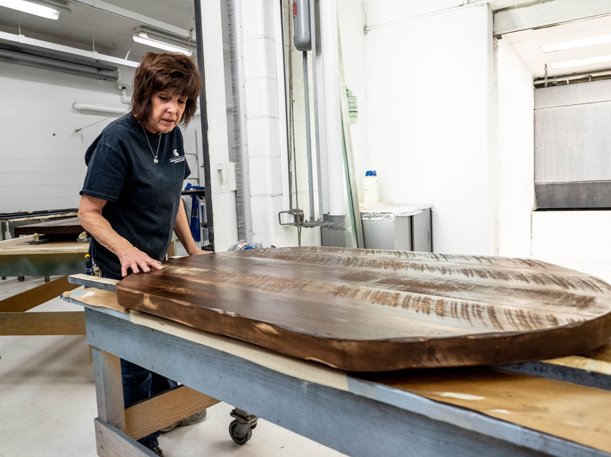 Photo of Pam Hebeler and a table top she is refinishing