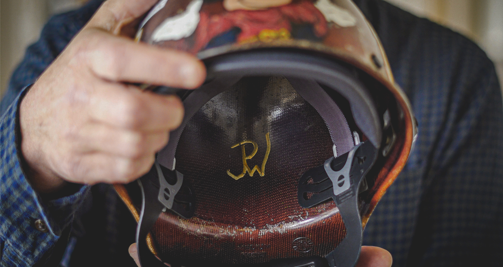 Todd Wilson holding his father's hard hat upside down to show the interior initials of his father