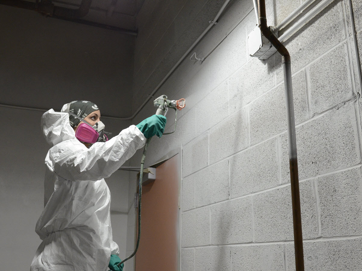 Photo of Jessica Partain spray painting in a campus mechanical room