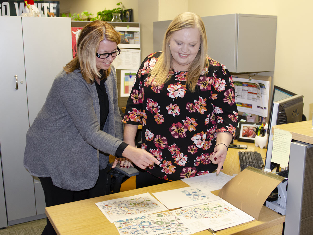 Photo of Angie Zell and Jamie Talbert in their office going over plans for an upcoming event, pre COVID outbreak