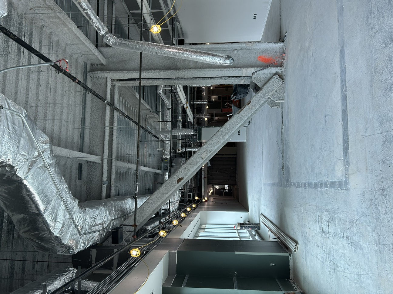 interior construction with a large expanse of concrete floor and large metal girders coated in fire retardant