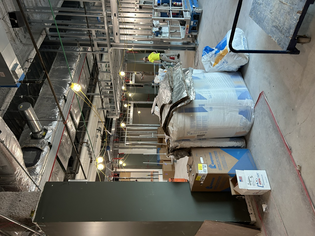 interior construction site with bales of insulation, exposed steel infrastructure and construction lights
