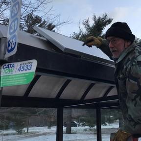Photo of IPF's Don Meyer attaching solar panel to top of CATA bus shelter