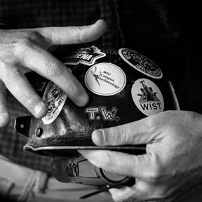 Photo of IPF's Todd Wilson's hands holding his hard hat adorned with various stickers and painted with his initials