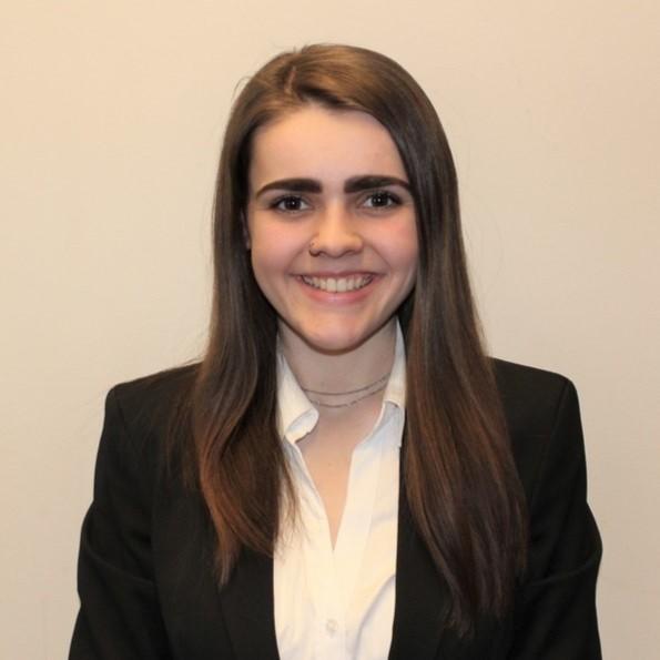 A young white woman with long brown hair in a white collared shirt and black blazer smiles at the camera