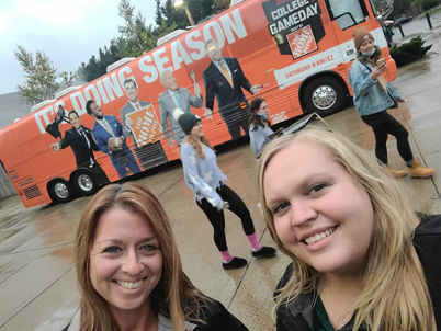 Angie Zell and Jamie Talbert smile in front of a gameday bus.