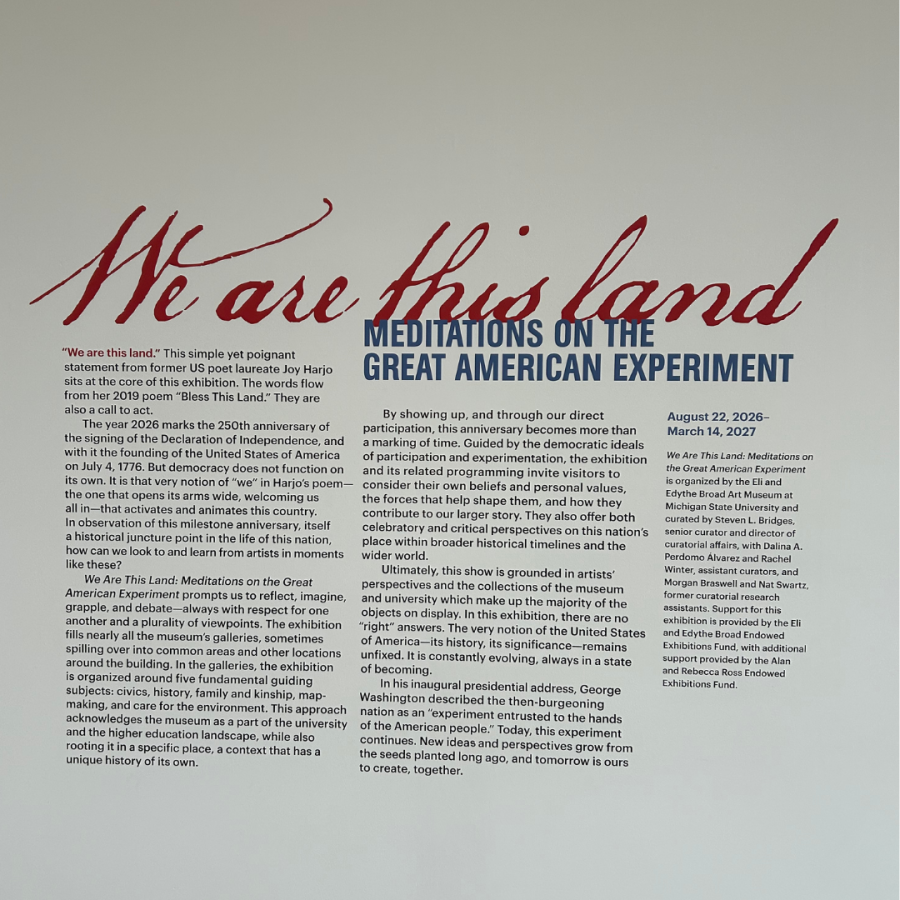 Descriptive words on the museum wall describing the exhibit features a sign reading “WE ARE THIS LAND.”