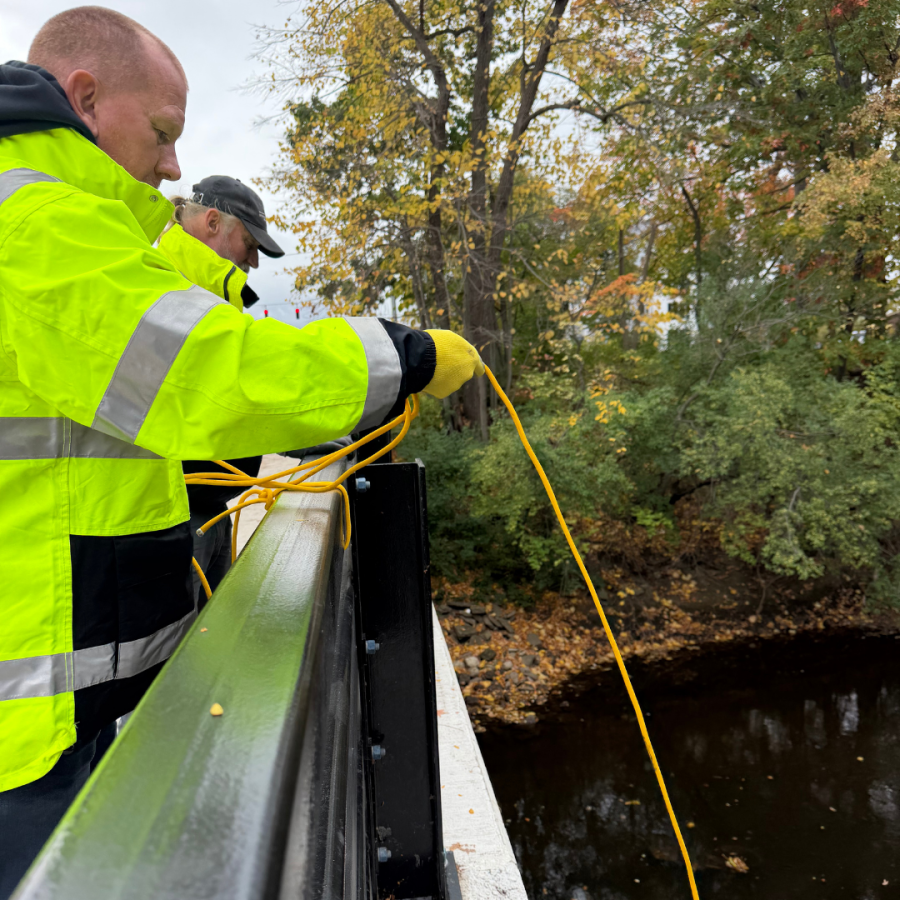 Man in a yellow safety vest holding a magnet on a bridge.
