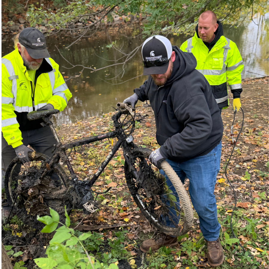 Three people wearing safety vests working on a bicycle.