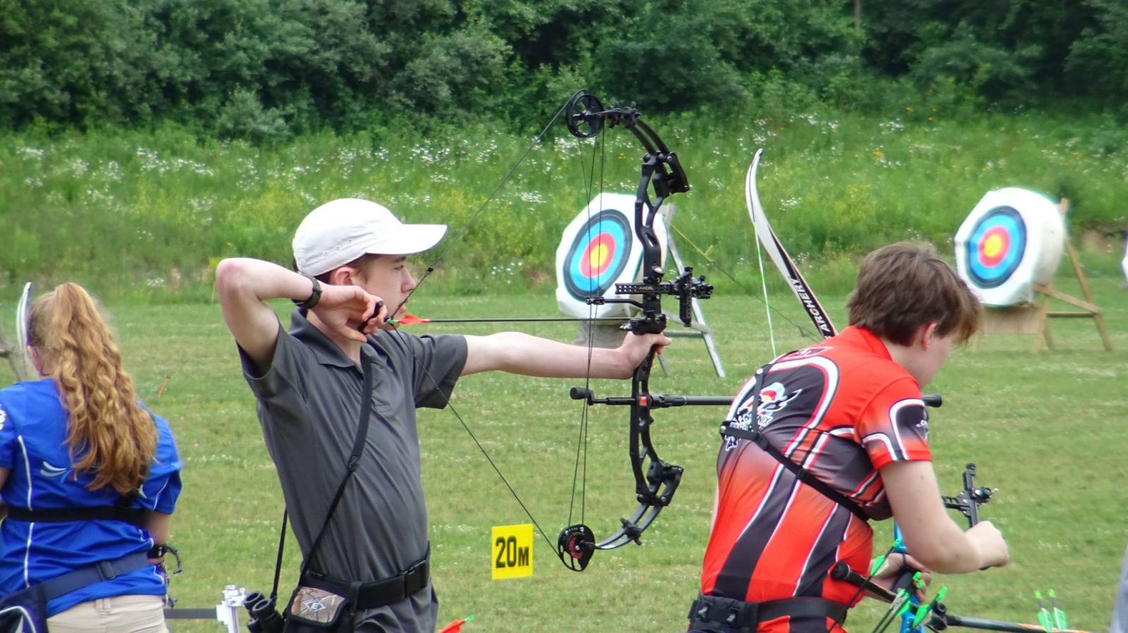 Man pointing bow at outdoor archery target