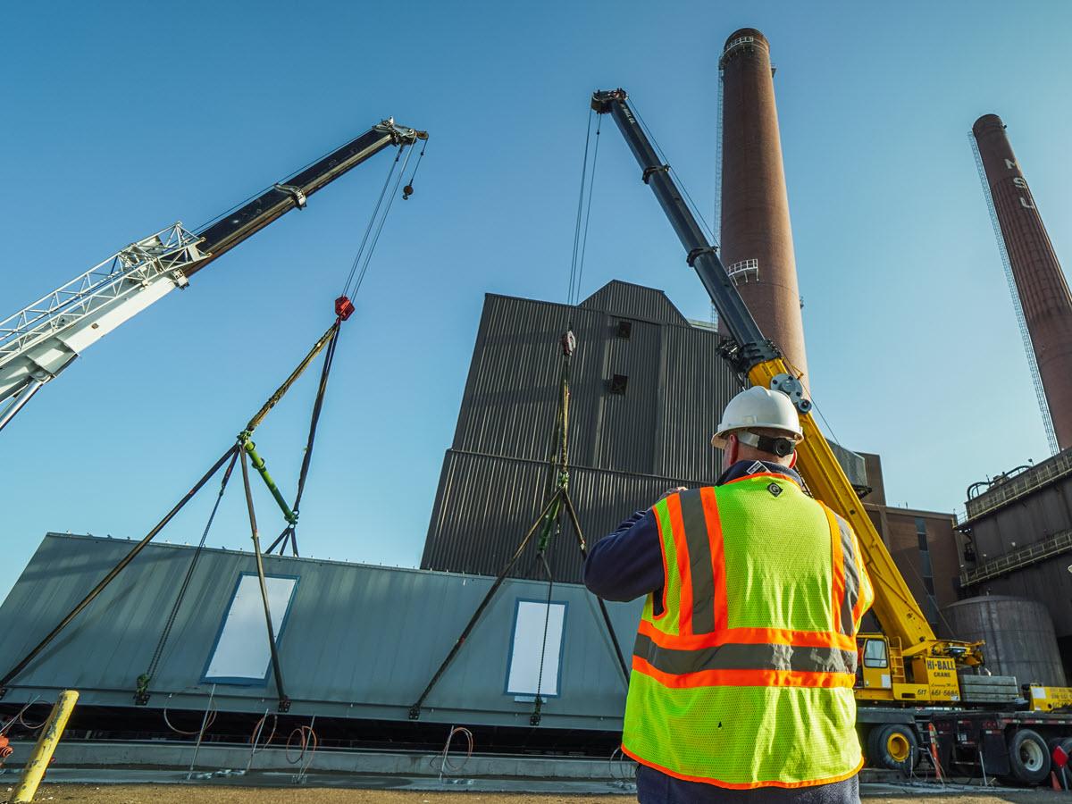 IPF high voltage crew member looking on as cranes lower the e-house into position