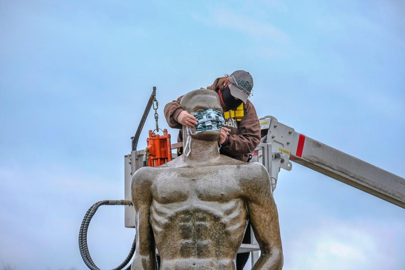 Landscape Services utility worker Kimberly Consavage putting a mask on the Sparty statue