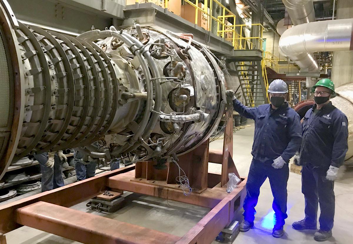 T.B. Simon Power Plant mechanics Michael Thiry and Reginald Buckland standing next to the Power Plant #6 combustion turbine generator 