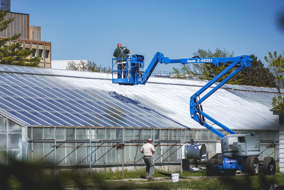 IPF's Mike McPherson using a lift and paint sprayer to apply shading concentrate to a greenhouse.