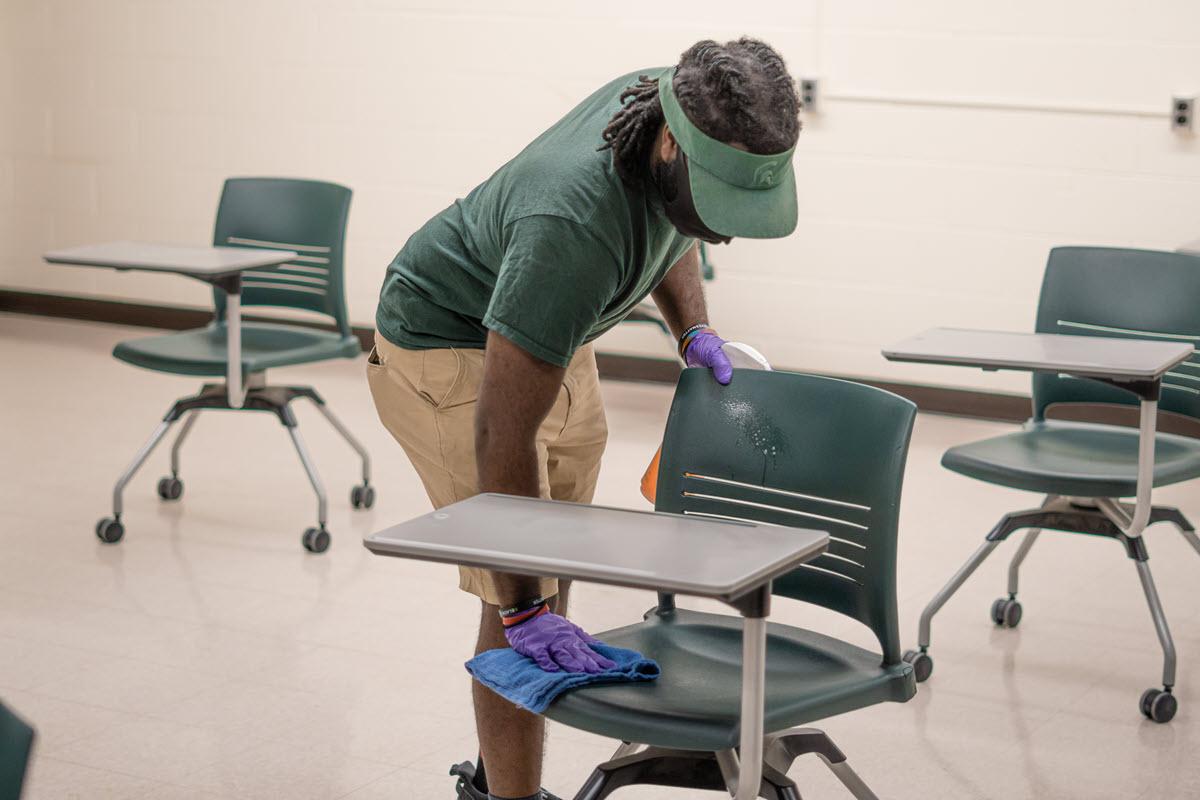 Photo of IPF custodian cleaning student desk in Wells Hall