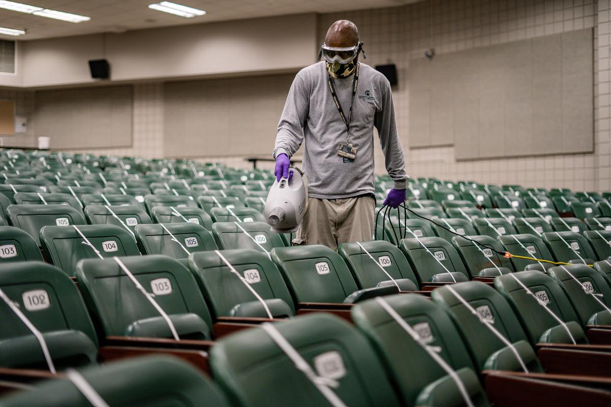 An IPF custodian operates one of the portable disinfectant misting units in a Wells Hall lecture hall. 