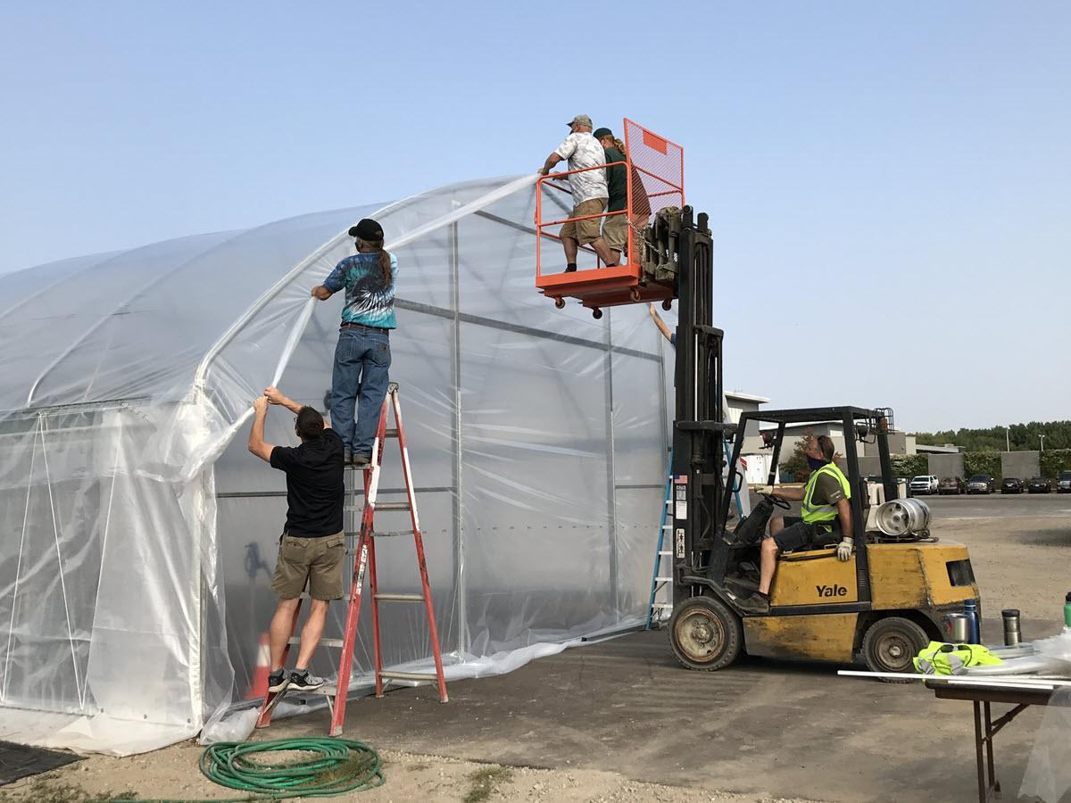 Recycling Center staff install the plastic cover over the new vermicomposting hoop house