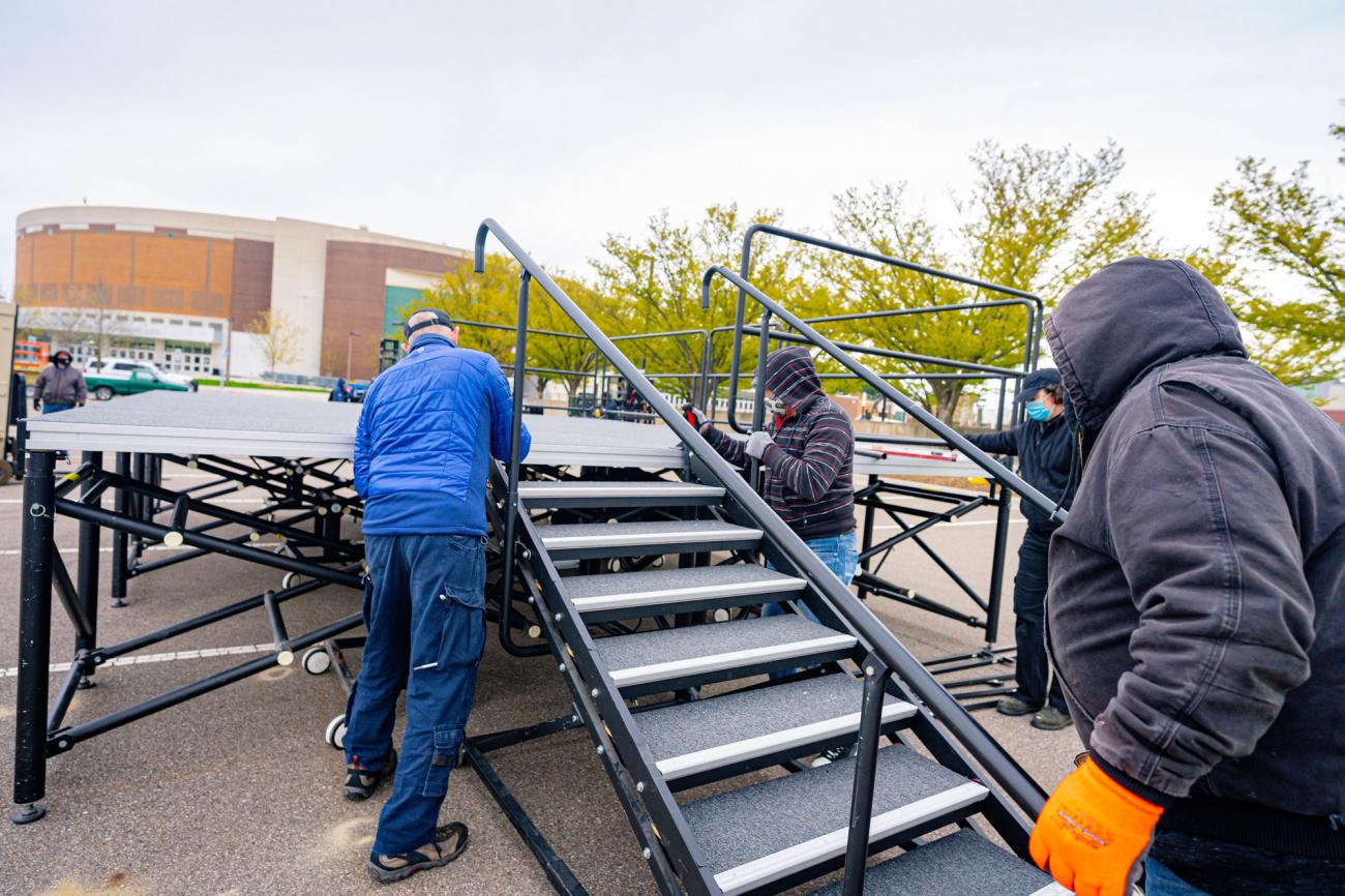 A crew attaches a staircase to an outdoor stage