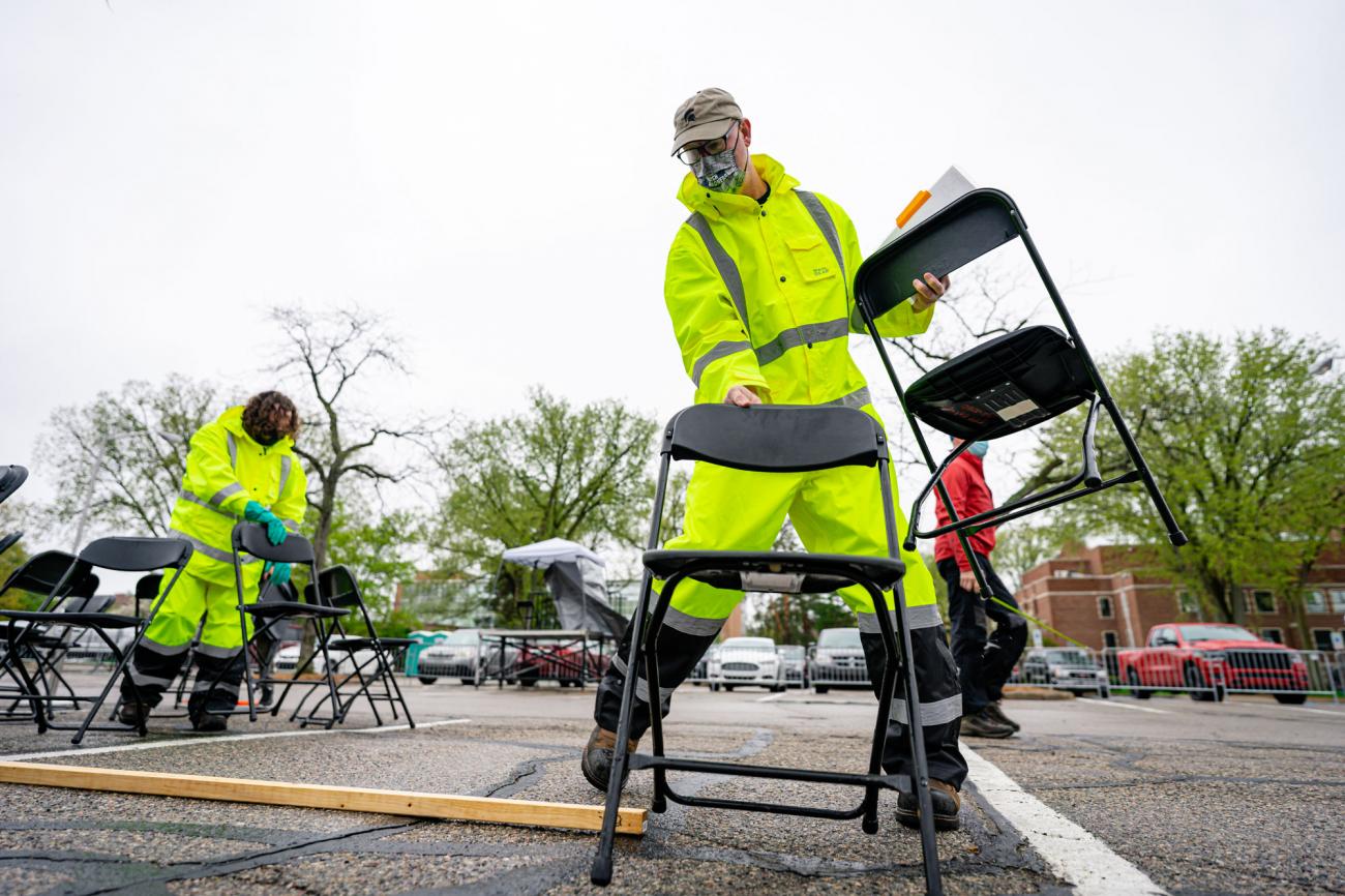 A man in a high-vis suit arranges chairs with a large measuring stick