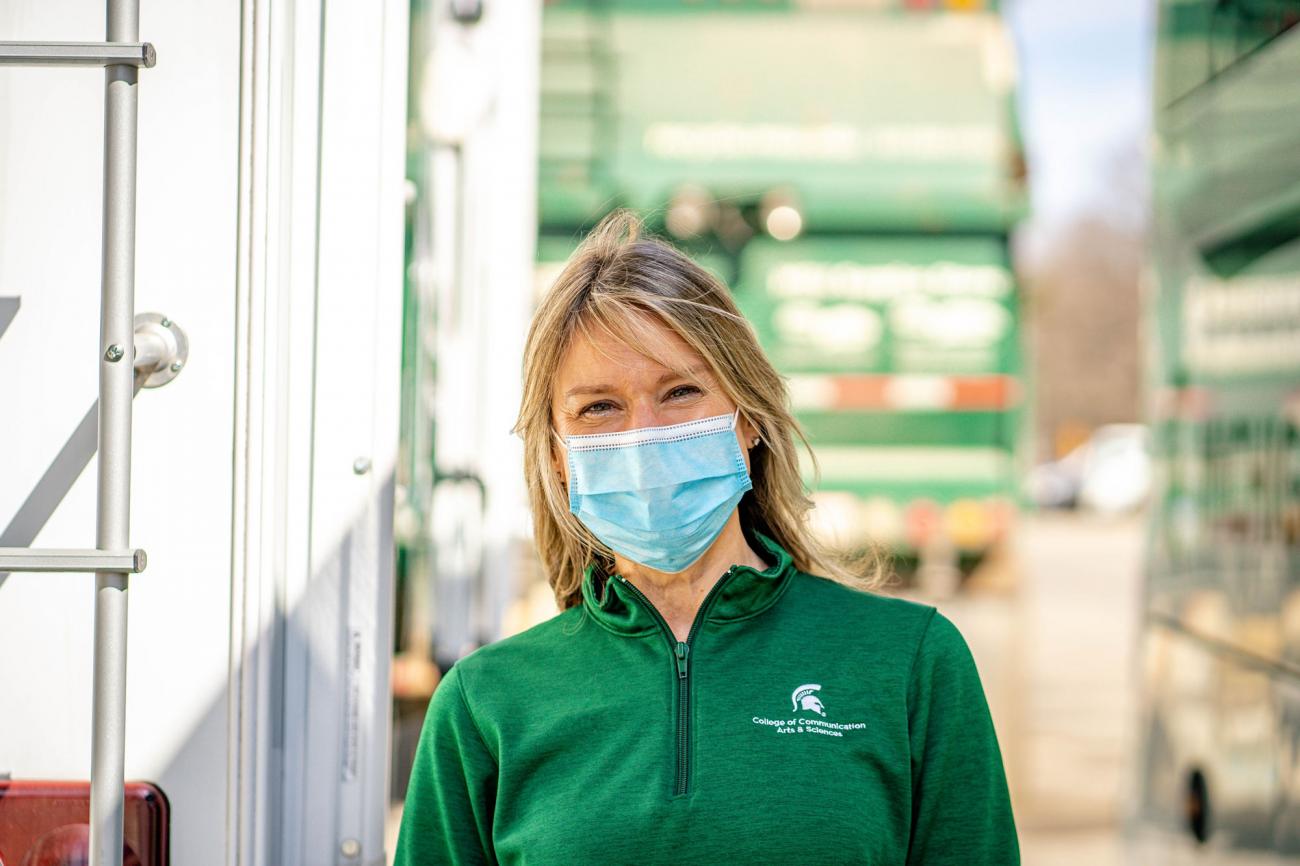 Blonde woman in a green MSU shirt and blue face covering.
