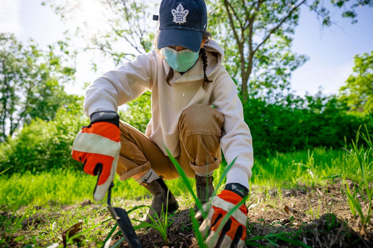 Sarah Naughtin with a trowel kneeling and planting a seedling