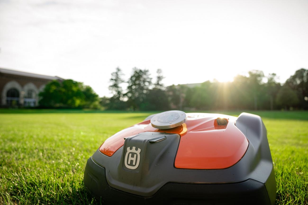 A small orange robot on wheels trundles along on green grass