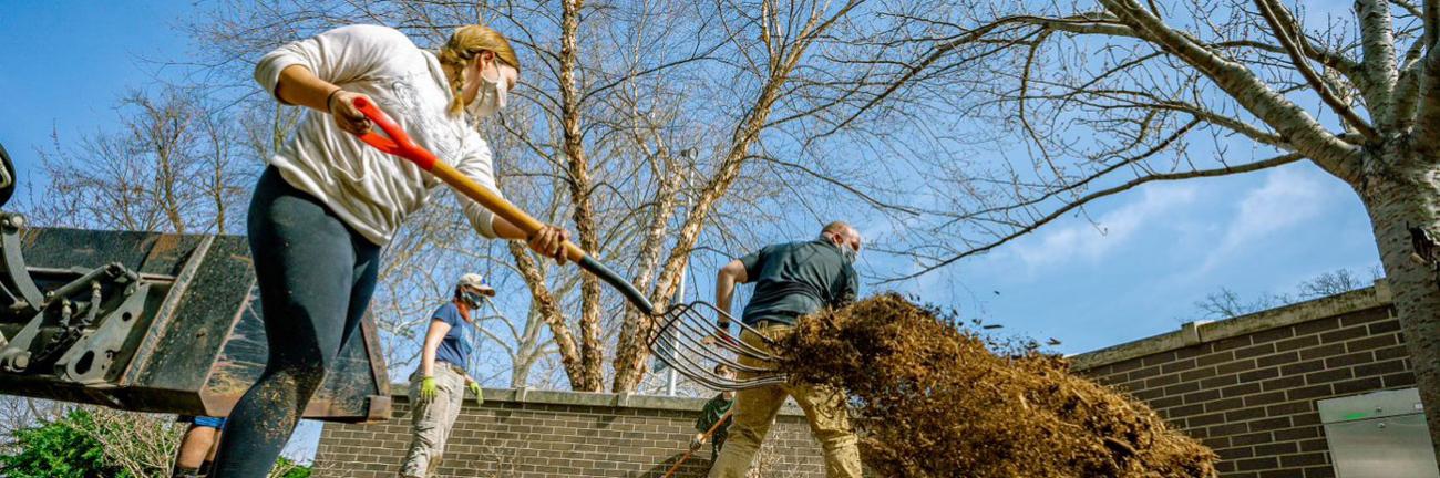 A student moves mulch with a large pitchfork