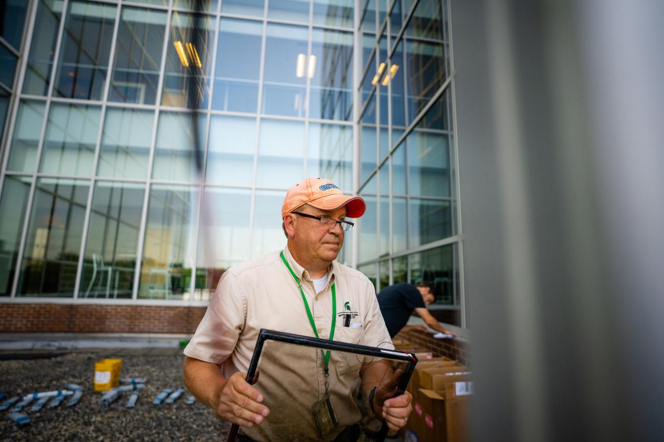 A man in an orange baseball cap carries a transparent pane to be installed.