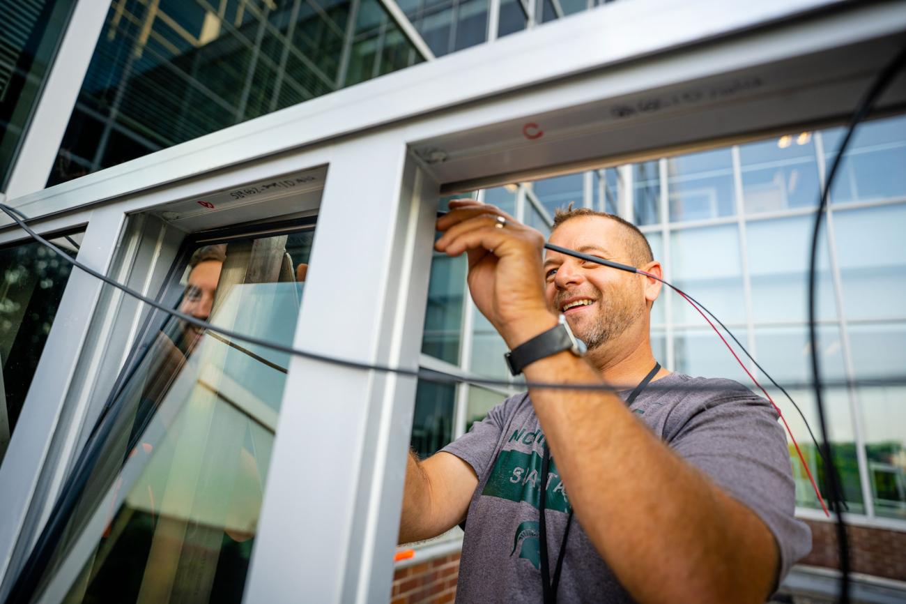 A man in a grey t-shirt works on wiring for the transparent panels.