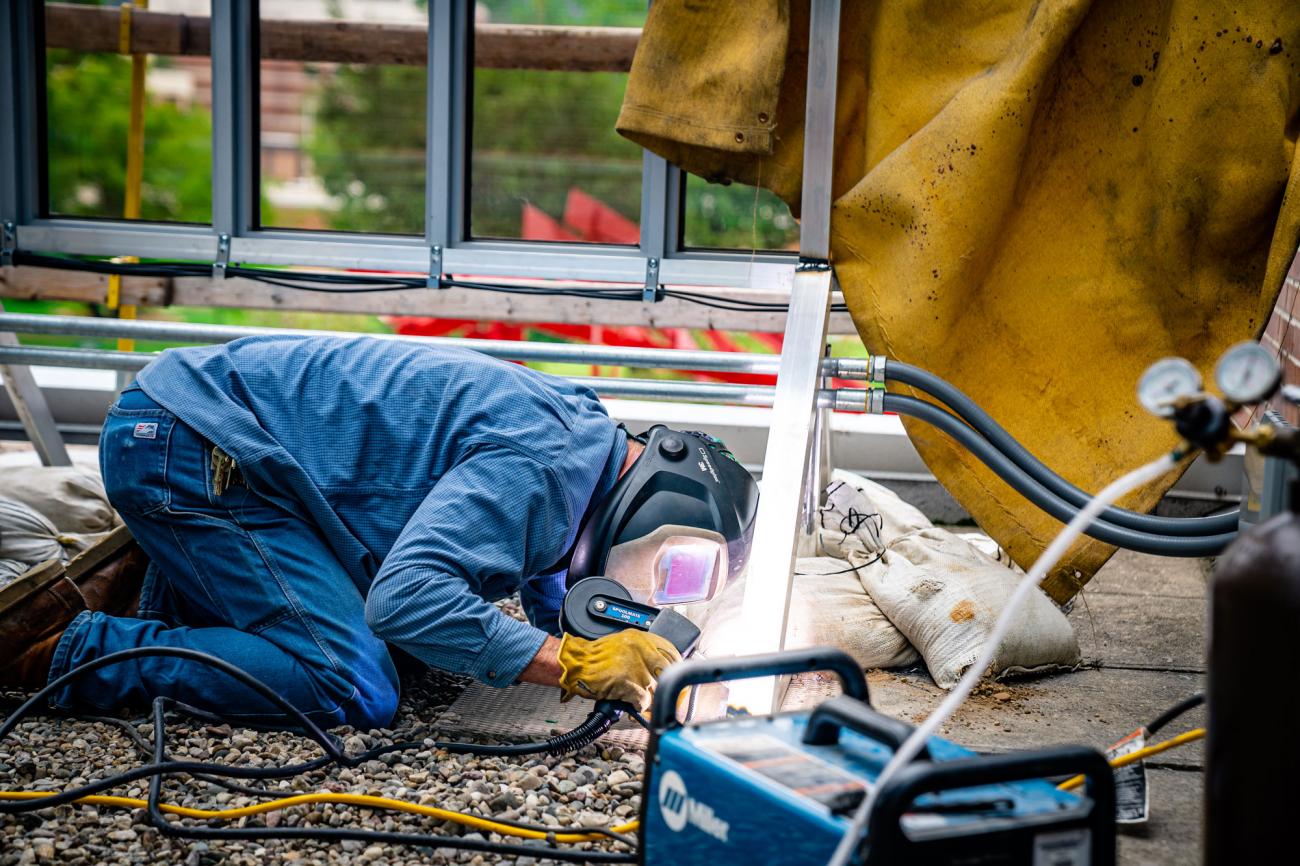 A welder wearing protective gear works on the metal frame for the solar panels.