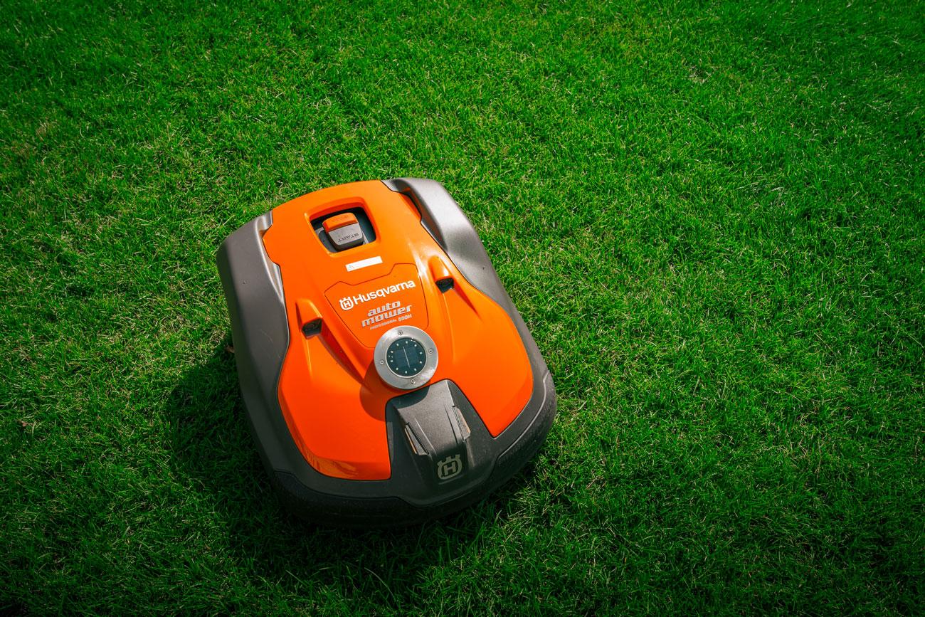 A squat Husqvarna mowing robot trundles along across green grass