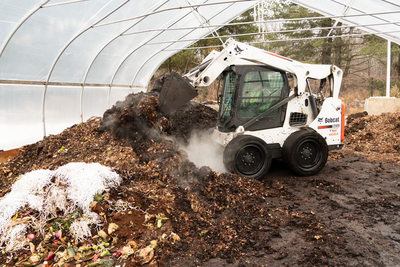 A staff member mixes leaves and food waste to make a pile of pre-compost worm food at the MSU Surplus Store and Recycling Center.