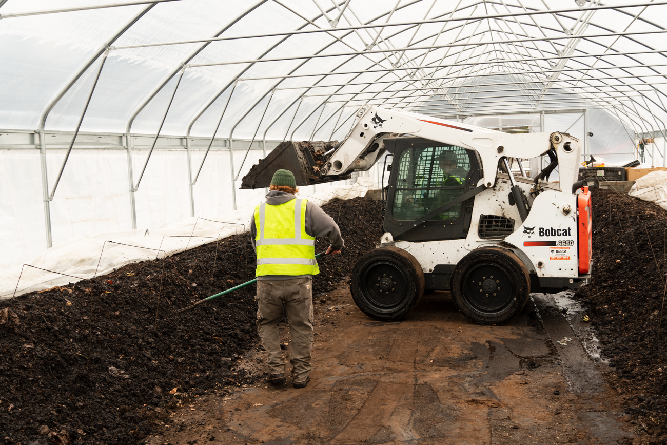 Staff members mix in new organic material to feed the worms in the compost rows.