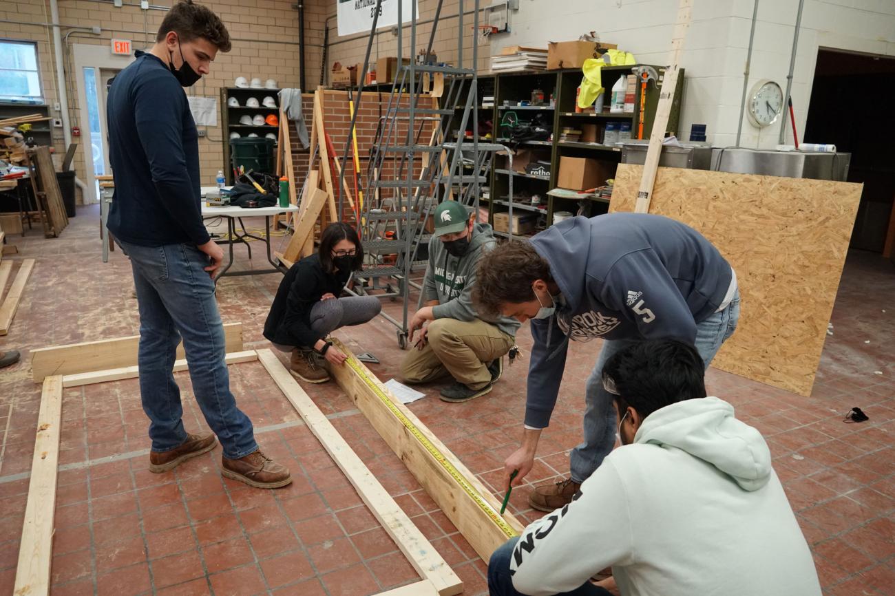 Four students work with Brandon Kibbey to measure a long 2"x4".