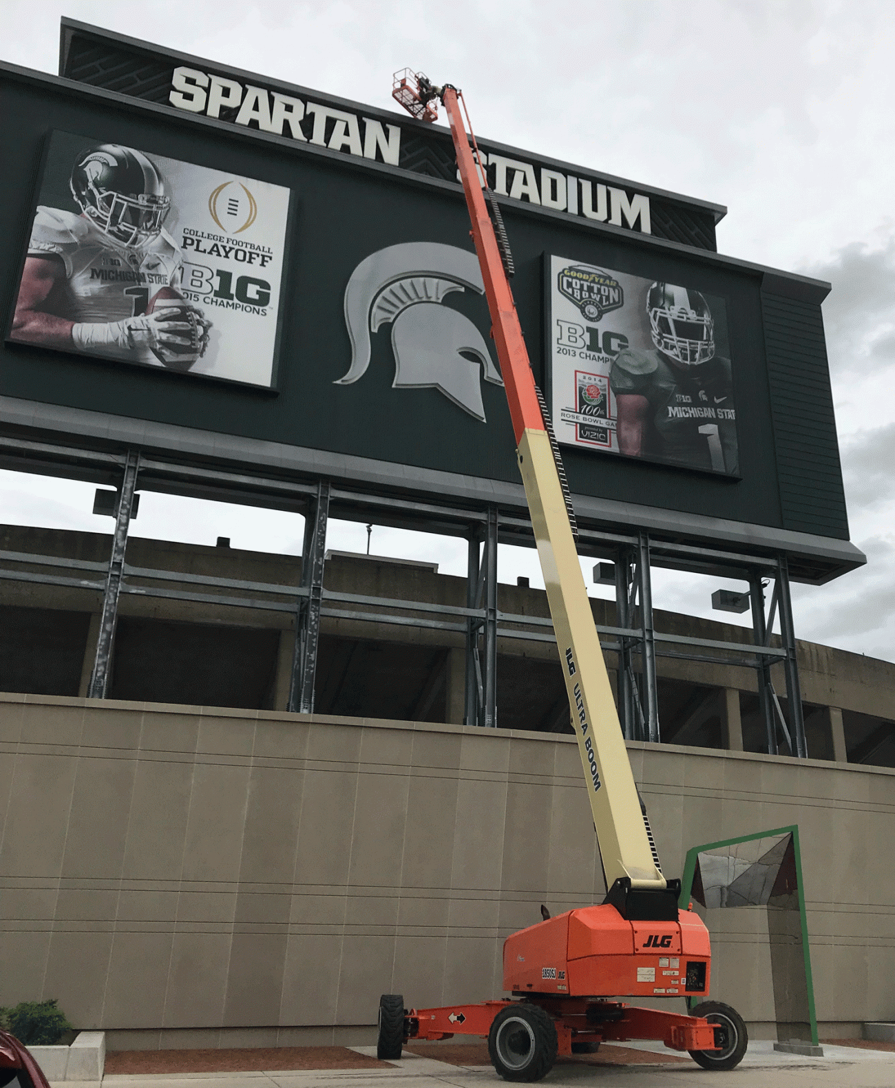 a large lift extends from the concrete ground to the top of the Spartan Stadium scoreboard