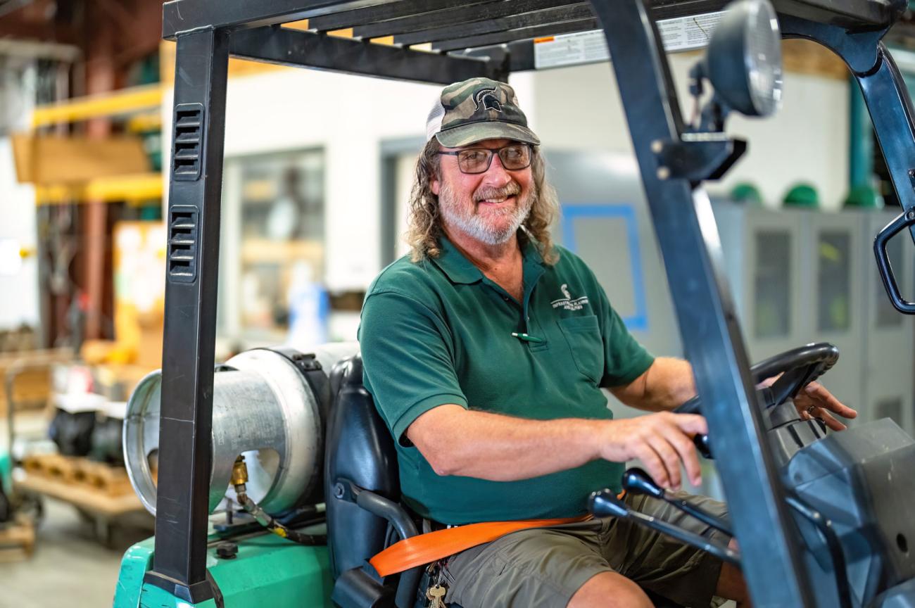 A smiling man is seated in a warehouse forklift vehicle