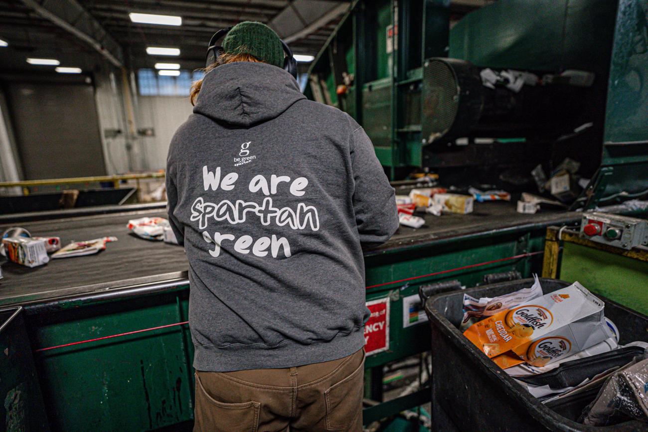 A worker sorts recyclables with a hoodie that reads "We are Spartan green"