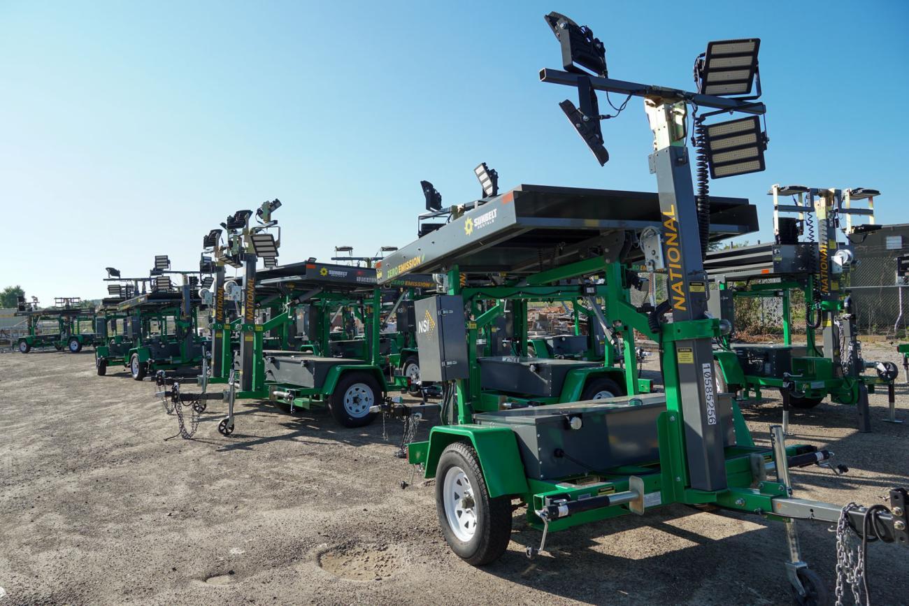 Large light towers lined up in an open dirt area.