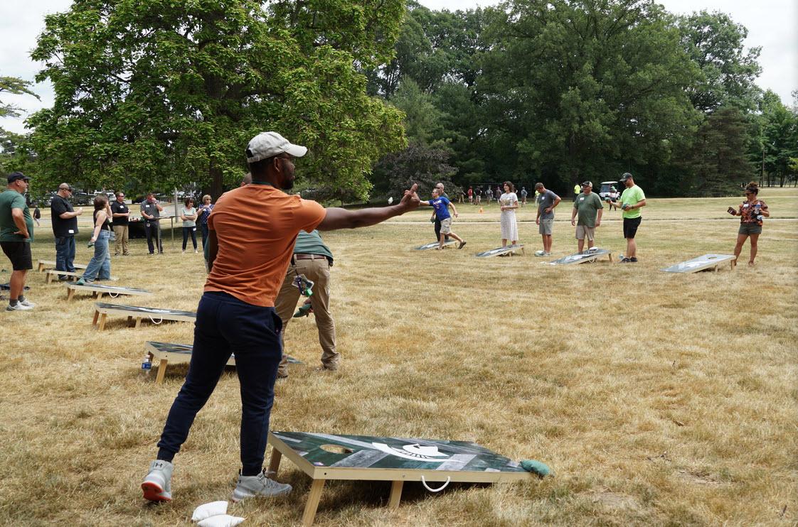 A long row of people toss beanbags toward the cornhole board yards away.