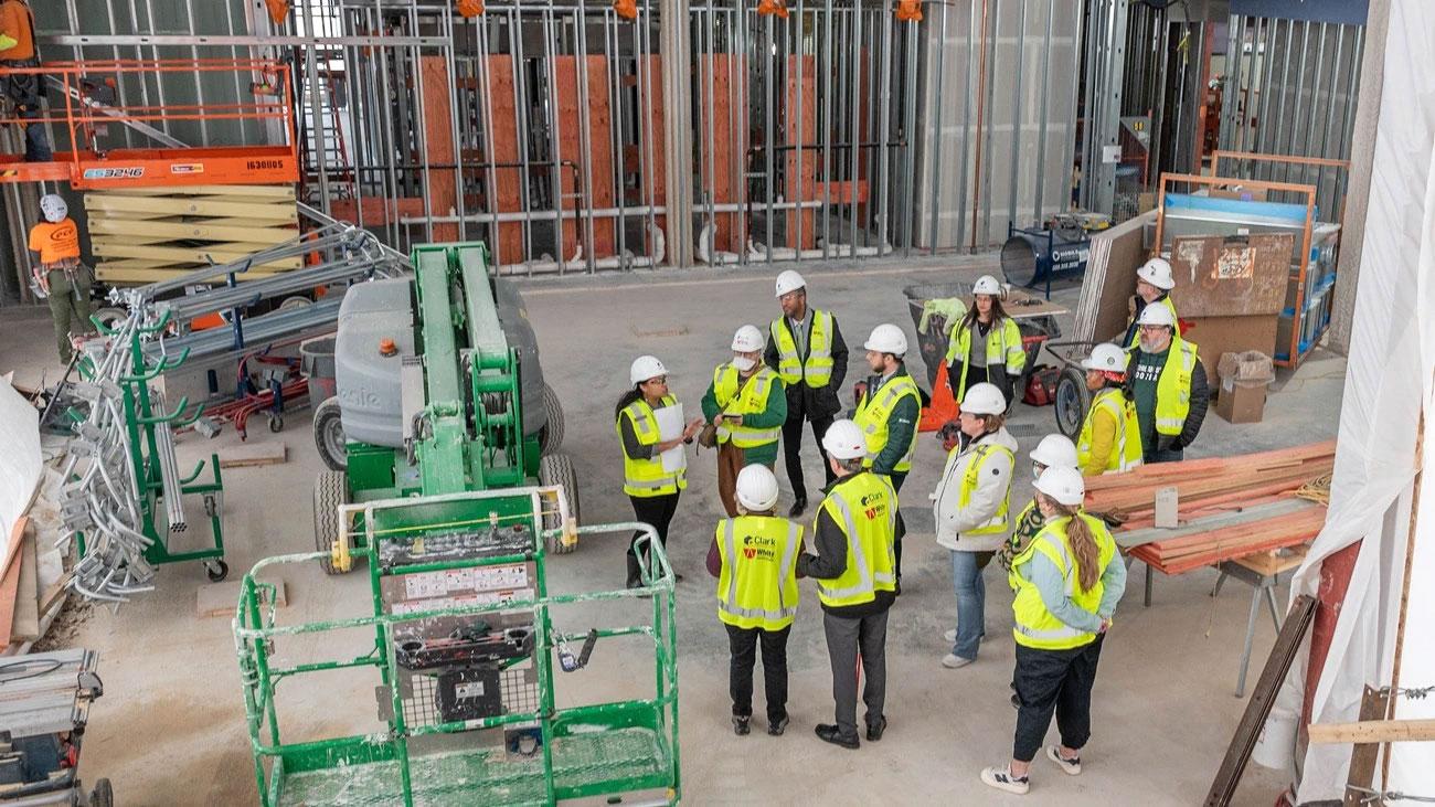A group of people in high-vis vests and hardhats tour an interior building construction area