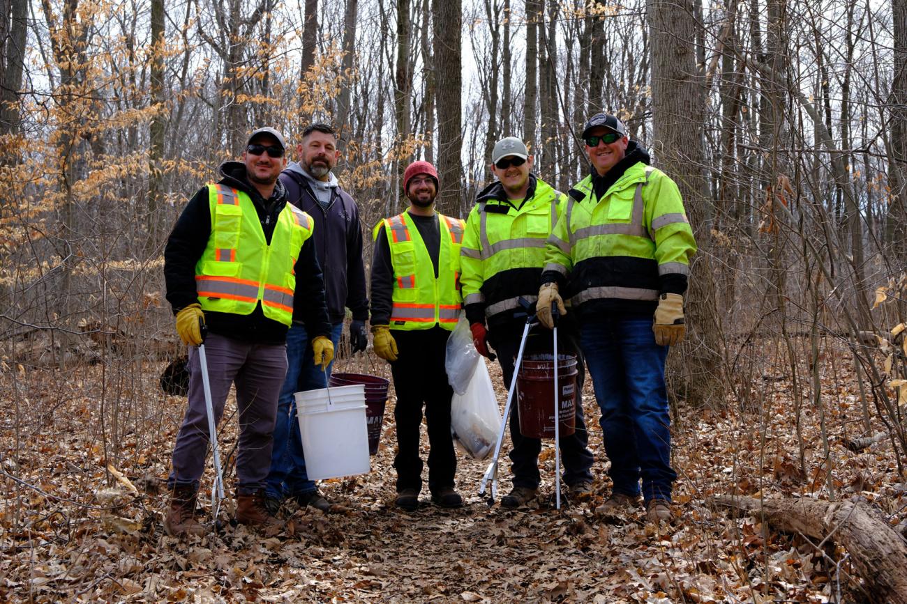 IPF employees stand with buckets and grabbers to collect trash and debris.