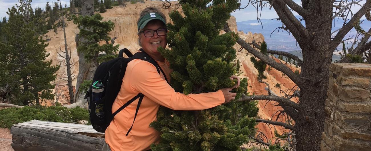 Photo of carolyn miller hugging a pine tree