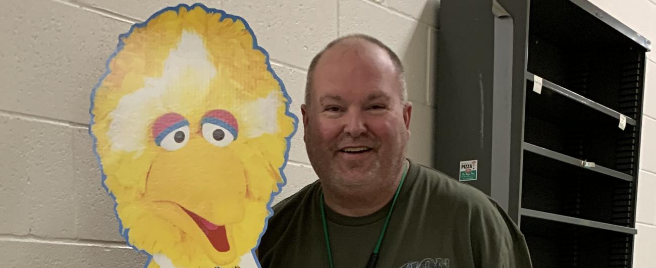 Mike Ouderkirk standing with a Sesame Street Big Bird cut out in the Comm Arts building