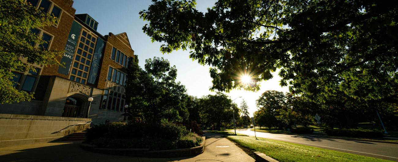 Angled photo of a campus building and street surrounded by trees late in the day