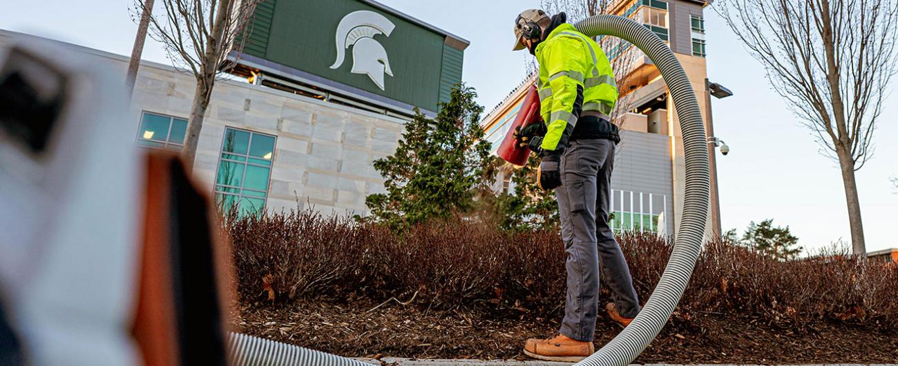 A landscape services worker blows mulch into a bed outside of Spartan Stadium
