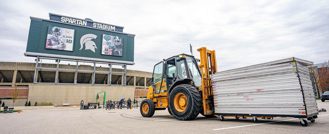 A forklift brings in parts of a disassembled stage in the Spartan Stadium parking lot